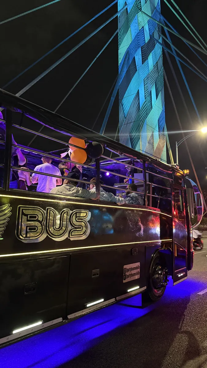 Bus del Tour Party Bus Medellín recorriendo la ciudad de noche con luces, música y ambiente festivo bajo el Puente de la 4 Sur